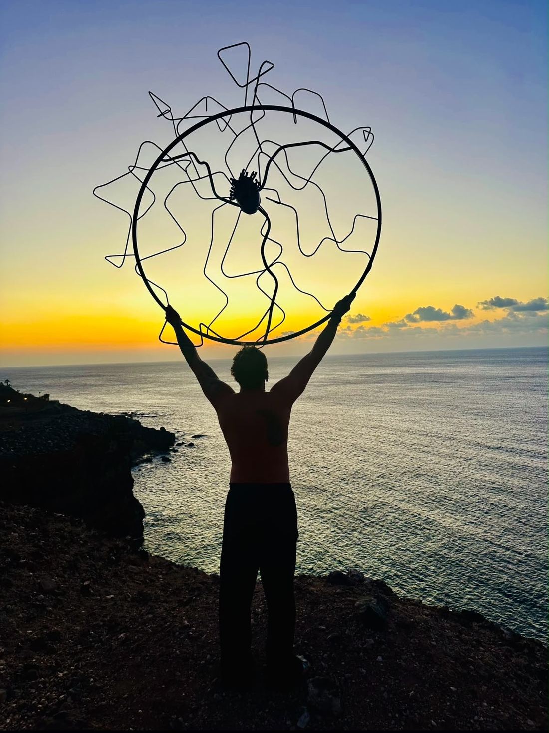 Escultura circular de acero sostenida frente al mar al atardecer