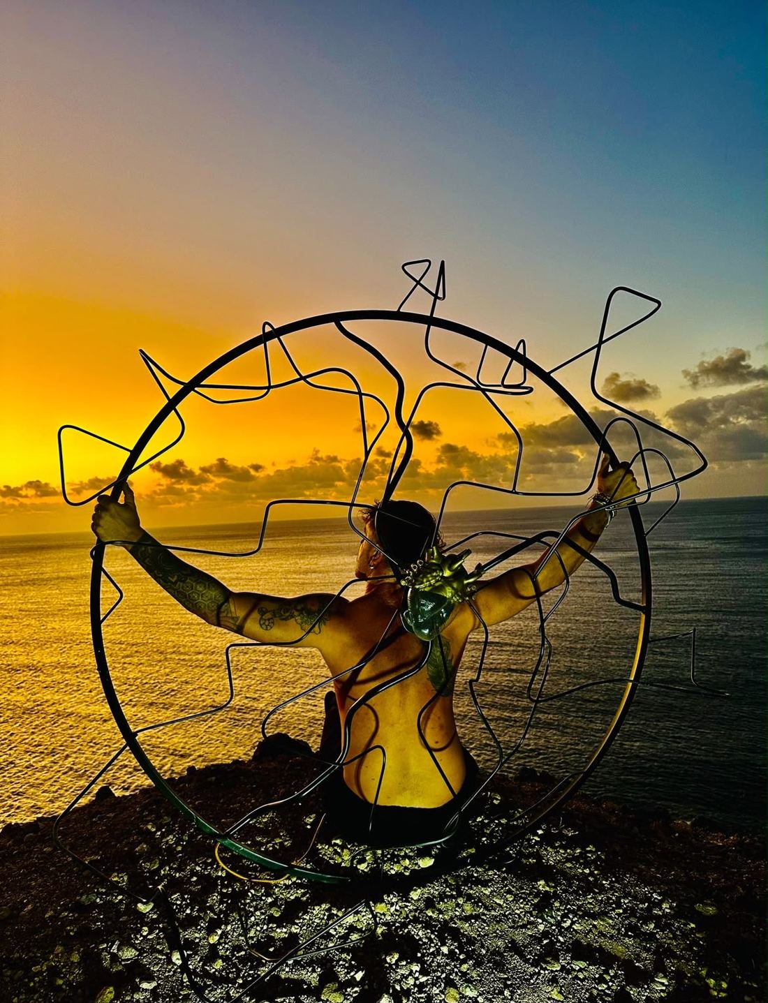 Escultura circular de acero sostenida frente al mar al atardecer